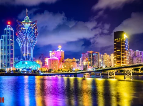 Night city skyline at dusk with neon-lit buildings, a curved glass tower, and a bright bridge over a reflective river.