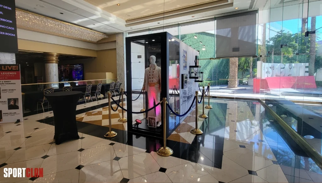 Одежда Элвиса Пресли - Лас-Вегас Mannequin in a white and gold costume inside a glass display case, roped off in a hotel lobby with a marble-style floor.