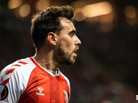 Side profile of a male soccer player wearing a red and white jersey on the field, focused and in action.