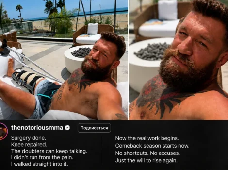 Bearded man with a knee brace relaxing on an outdoor lounge chair on a sunny terrace, beach in the background, tattoos visible on his chest and arm.