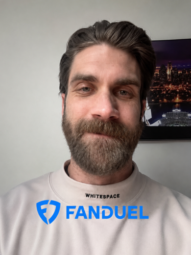 Close-up of a man with a beard taking a selfie; he wears a light sweatshirt with the word 'WHITESPACE' and a FANDUEL logo on the chest.