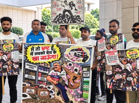 Group of men protest outside a government building, holding large illustrated posters about corruption and gun violence in India.