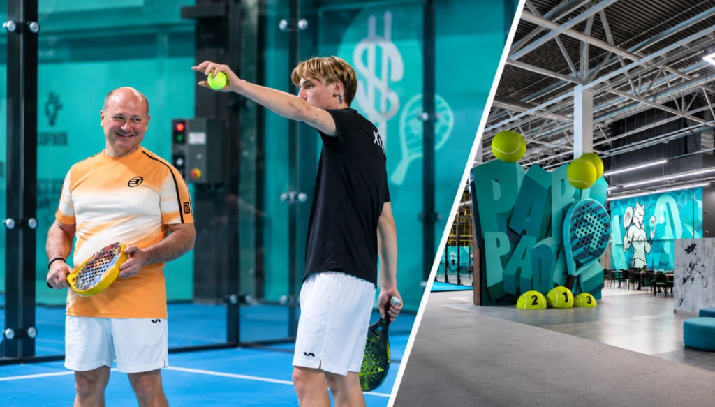 Two men playing padel indoors: one in orange shirt smiling, the other in black shirt shoots a ball while holding a racket.