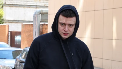 Young man in a black hoodie walking outdoors on a street, looking to his left.