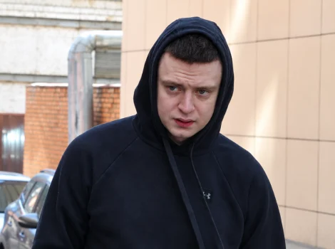 Young man in a black hoodie walking outdoors on a street, looking to his left.